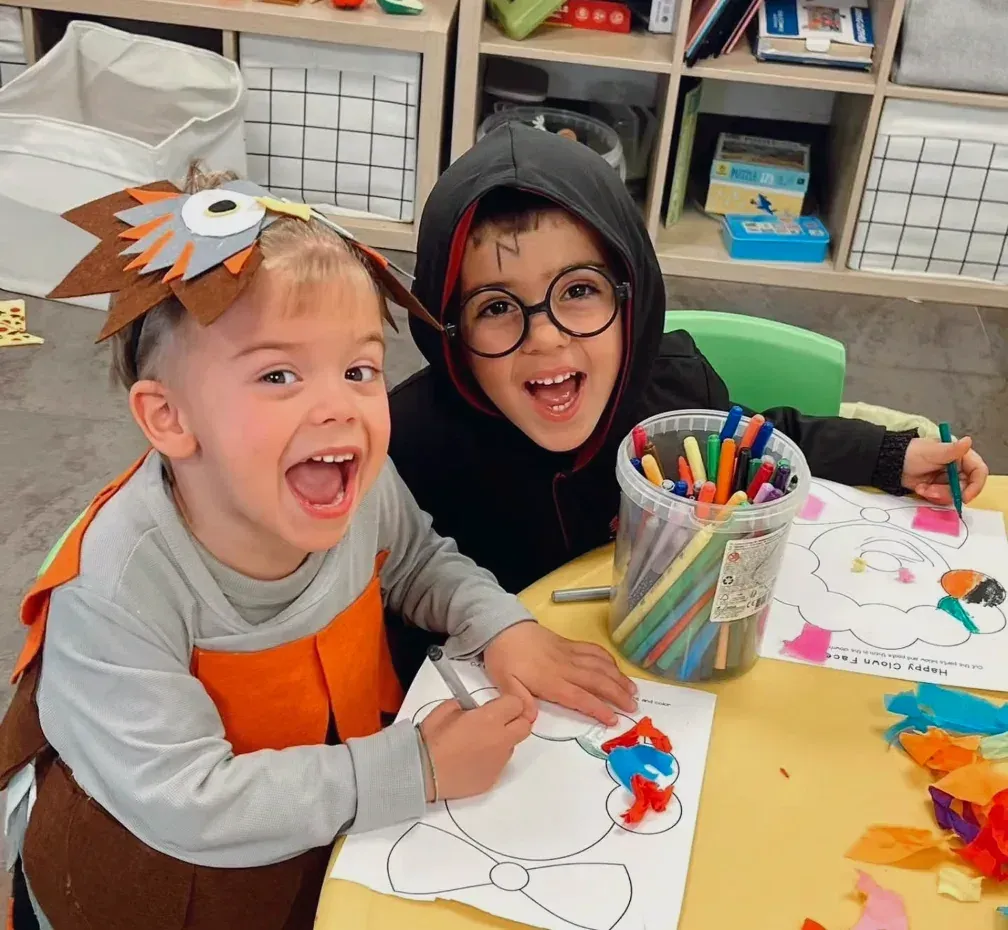 Dos nens disfressats pintant una fitxa a la taula de classe