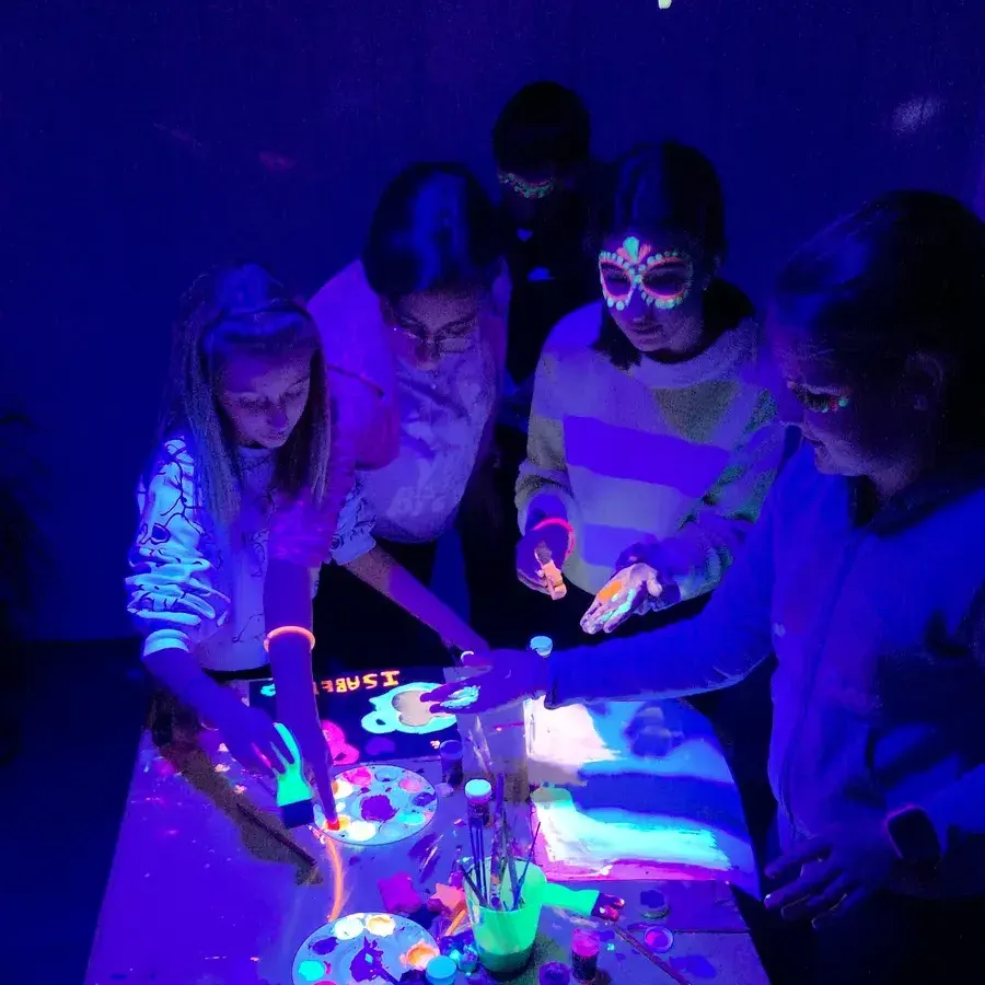 Alumnes pintant en un taller nocturn amb llum ultraviolada