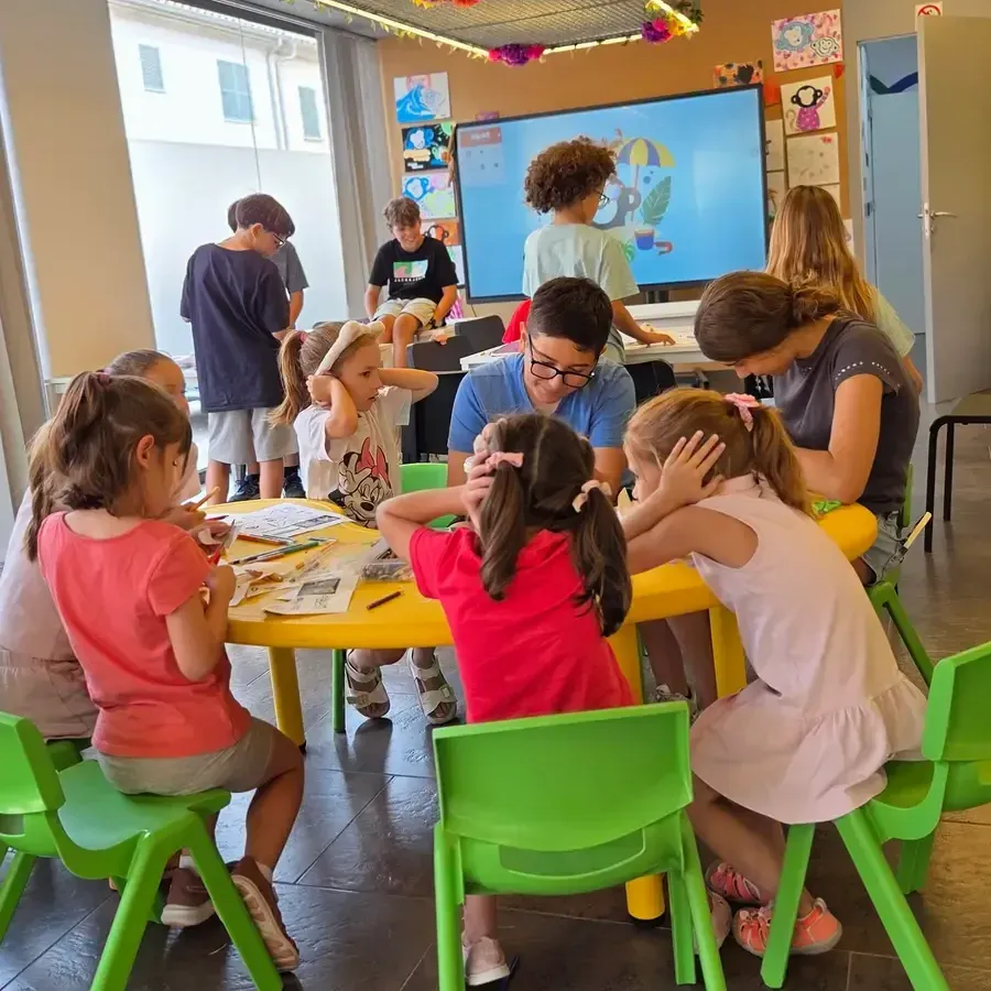 Nens dibuixant al voltant d'una taula groga al taller d'estiu